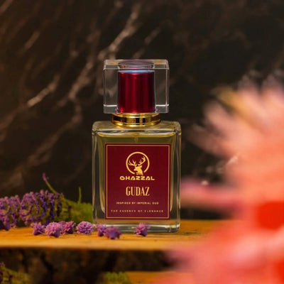 Perfume bottle labeled 'Gudaz' by Charral on a wooden surface with flowers in the background